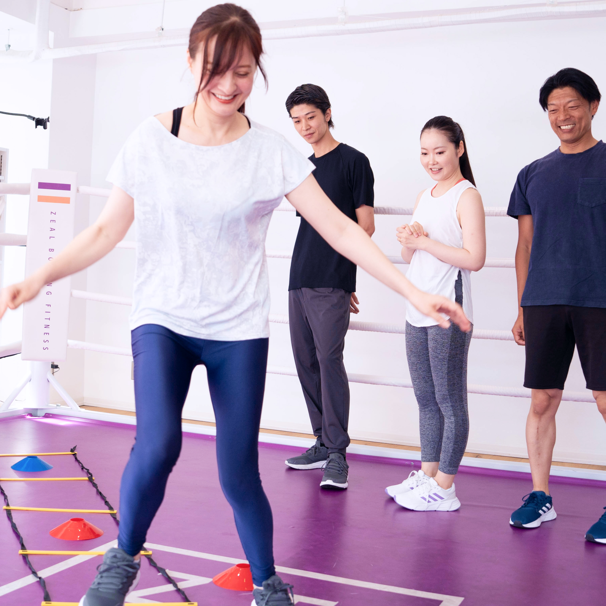 アジリティラダーを使ったトレーニングを指導するトレーナーと、それを見守る参加者の様子