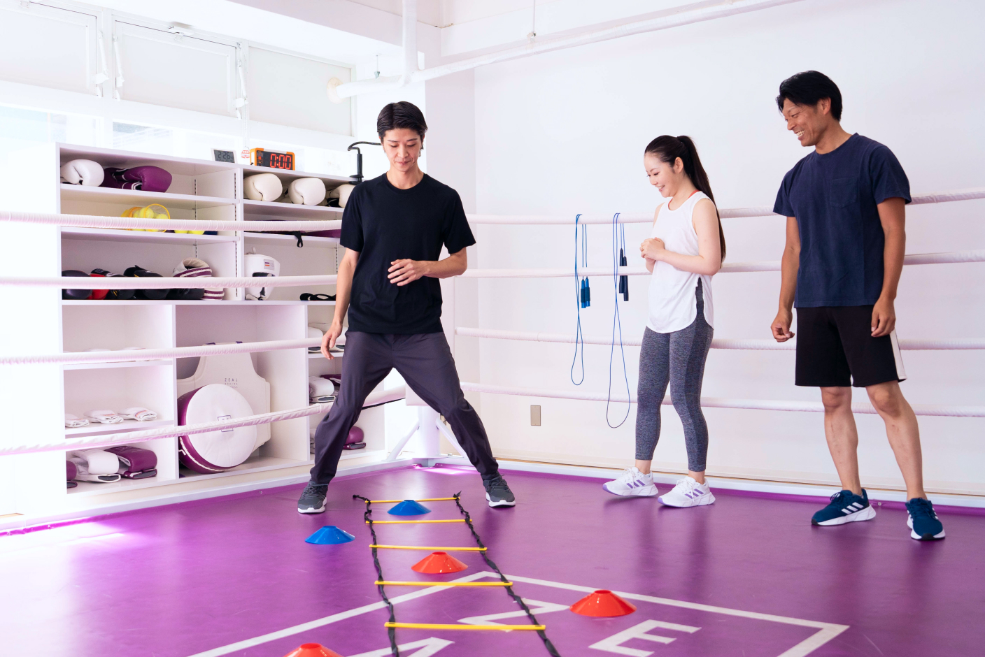 アジリティラダーを使ったトレーニングを指導するトレーナーと、それを見守る参加者の様子