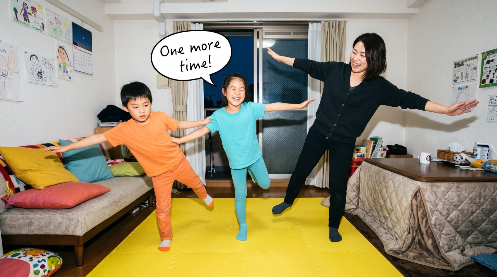冬の夜、リビングのマットの上で、片足立ちのポーズで遊ぶお母さんと子どもたち（イメージ）