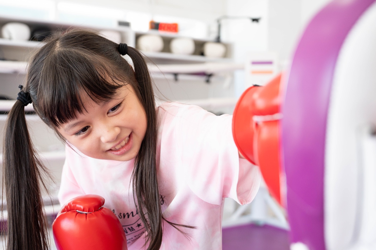 笑顔の小学生が明るいスタジオでコーチのミットにパンチし、奥で友達がラダーゲームをしているEnglish Fight Kidsのノンコンタクト指導風景